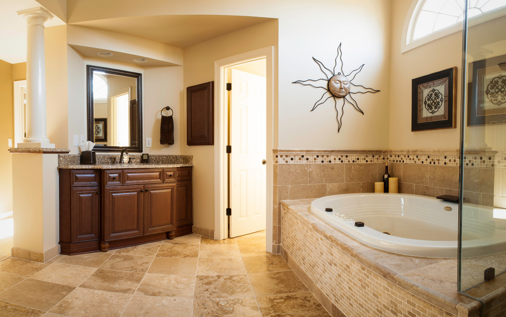 Réalisation d'une salle de bain principale tradition en bois brun avec un lavabo intégré, un placard avec porte à panneau surélevé, un plan de toilette en granite, une baignoire posée, une douche d'angle, un carrelage beige, un carrelage de pierre, un mur beige et un sol en calcaire.