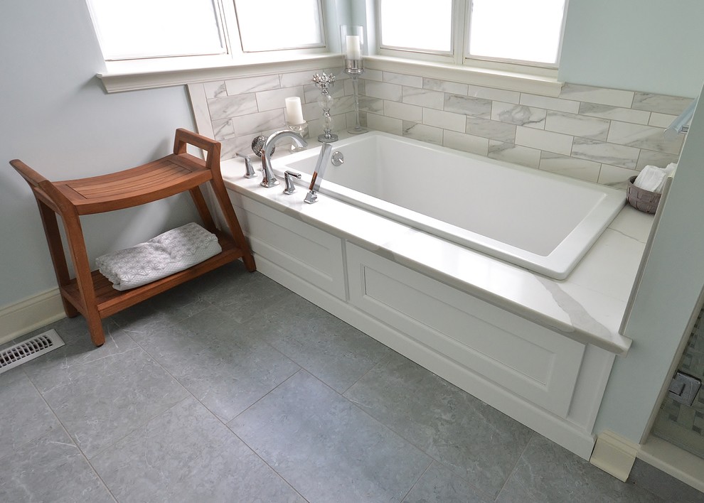 Пример оригинального дизайна: большая главная ванная комната в стиле неоклассика (современная классика) с плоскими фасадами, белыми фасадами, полновстраиваемой ванной, угловым душем, унитазом-моноблоком, белой плиткой, плиткой кабанчик, белыми стенами, полом из керамической плитки, врезной раковиной, столешницей из искусственного кварца, серым полом, душем с распашными дверями и белой столешницей