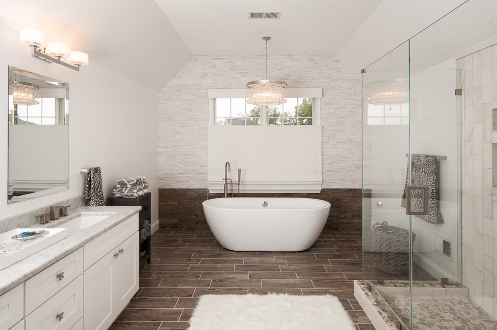 Cette photo montre une grande salle de bain principale chic avec un lavabo encastré, un placard à porte shaker, des portes de placard blanches, une baignoire indépendante, un mur gris, une douche d'angle, un carrelage blanc et un sol marron.