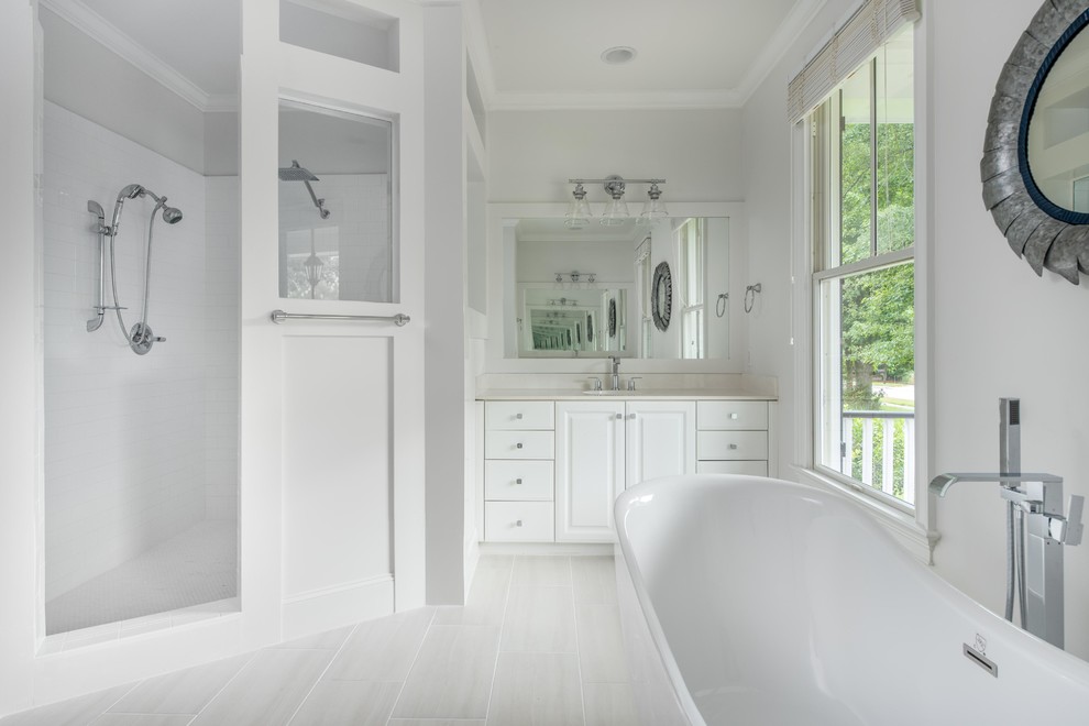 Photo of a large modern ensuite bathroom in Charleston with raised-panel cabinets, white cabinets, a freestanding bath, a double shower, a one-piece toilet, white tiles, porcelain tiles, white walls, porcelain flooring, a built-in sink, engineered stone worktops, white floors, a hinged door and white worktops.