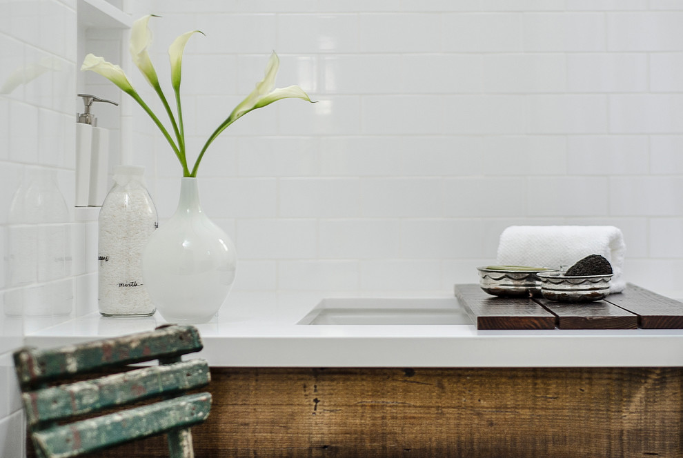 Klassisk inredning av ett litet en-suite badrum, med ett undermonterat badkar, en dusch/badkar-kombination, en toalettstol med separat cisternkåpa, vit kakel, tunnelbanekakel, vita väggar, marmorgolv, ett nedsänkt handfat, bänkskiva i akrylsten, släta luckor och skåp i slitet trä