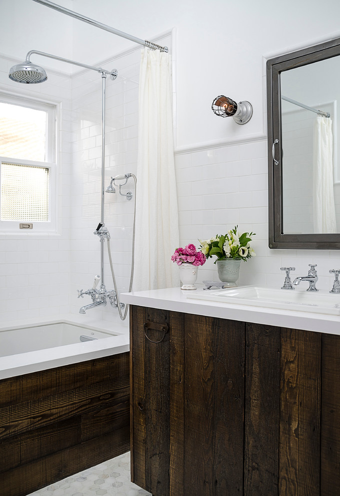Bild på ett litet vintage en-suite badrum, med ett nedsänkt handfat, ett undermonterat badkar, en dusch/badkar-kombination, vit kakel, tunnelbanekakel, bänkskiva i akrylsten, en toalettstol med separat cisternkåpa, vita väggar, marmorgolv, släta luckor, skåp i slitet trä och dusch med duschdraperi