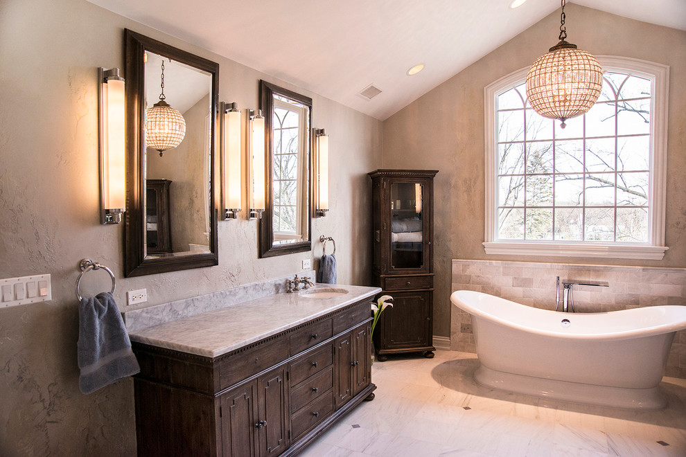 Inredning av ett klassiskt stort badrum, med ett undermonterad handfat, möbel-liknande, skåp i slitet trä, marmorbänkskiva, ett fristående badkar, gul kakel, stenkakel, flerfärgade väggar och marmorgolv