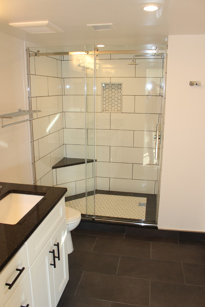 This is an example of a large modern ensuite bathroom in DC Metro with shaker cabinets, white cabinets, an alcove shower, a one-piece toilet, white tiles, porcelain tiles, white walls, porcelain flooring, a submerged sink, granite worktops, black floors and a sliding door.