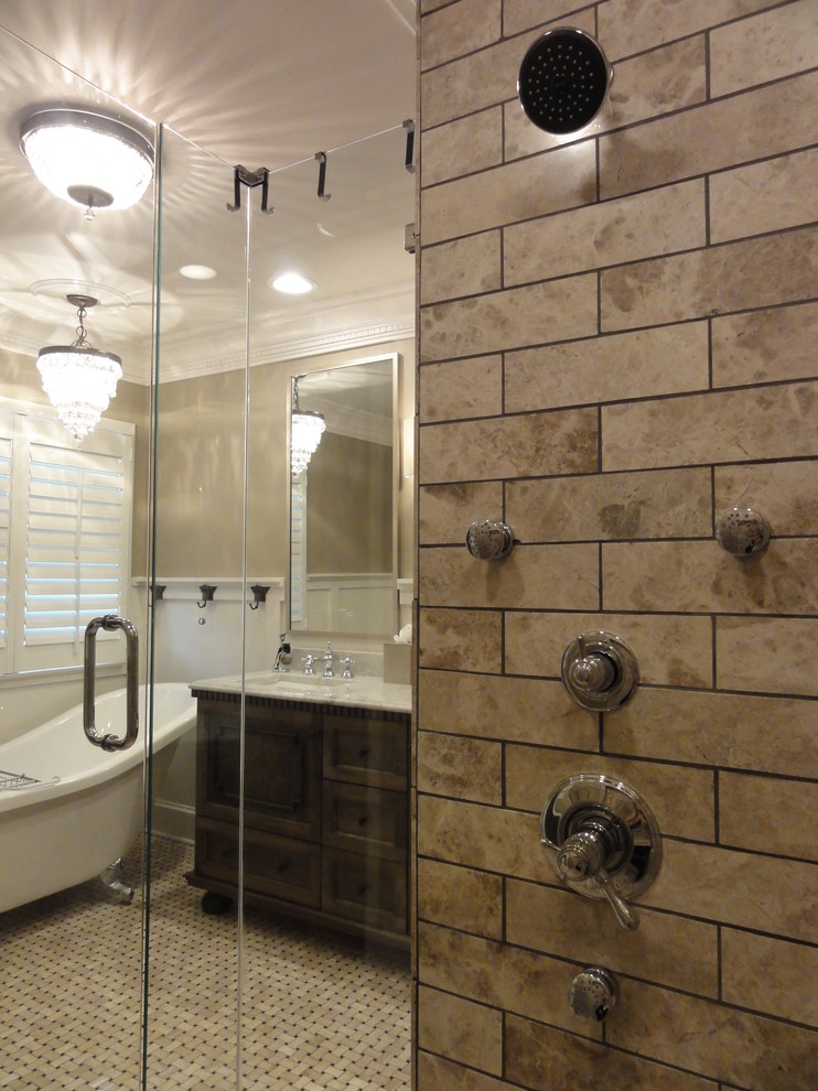 Klassisk inredning av ett badrum, med ett undermonterad handfat, möbel-liknande, skåp i mörkt trä, marmorbänkskiva, ett badkar med tassar, en dusch i en alkov, en toalettstol med separat cisternkåpa, beige kakel och mosaik