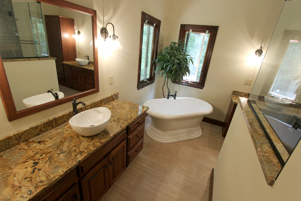 Photo of a large traditional bathroom in Cleveland with a vessel sink, raised-panel cabinets, dark wood cabinets, granite worktops, a corner shower, beige tiles, porcelain tiles, yellow walls and porcelain flooring.