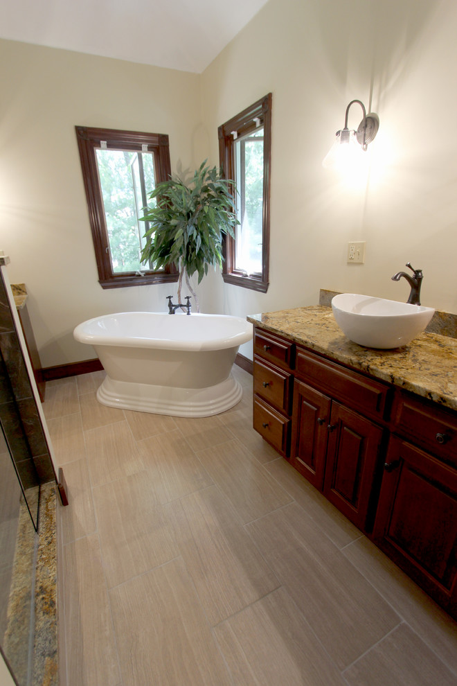 Cette image montre une grande salle de bain traditionnelle en bois foncé avec une vasque, un placard avec porte à panneau surélevé, un plan de toilette en granite, une douche d'angle, un carrelage beige, des carreaux de porcelaine, un mur jaune et un sol en carrelage de porcelaine.
