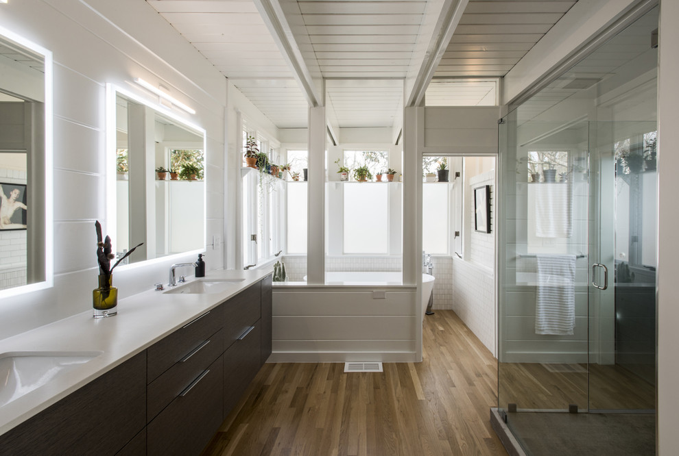 Идея дизайна: главная ванная комната в стиле ретро с плоскими фасадами, серыми фасадами, отдельно стоящей ванной, белой плиткой, керамической плиткой, белыми стенами, паркетным полом среднего тона, врезной раковиной, столешницей из искусственного кварца и белой столешницей