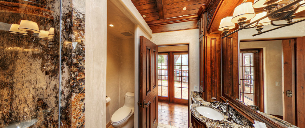 Design ideas for a medium sized mediterranean ensuite bathroom in San Francisco with a built-in sink, raised-panel cabinets, dark wood cabinets, granite worktops, a corner shower, a one-piece toilet, beige tiles, stone tiles, beige walls and travertine flooring.