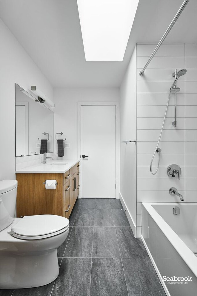 Inspiration for a medium sized contemporary ensuite bathroom in Vancouver with flat-panel cabinets, light wood cabinets, a built-in bath, a shower/bath combination, a one-piece toilet, white tiles, white walls, porcelain flooring, a submerged sink, engineered stone worktops, grey floors, a shower curtain and white worktops.