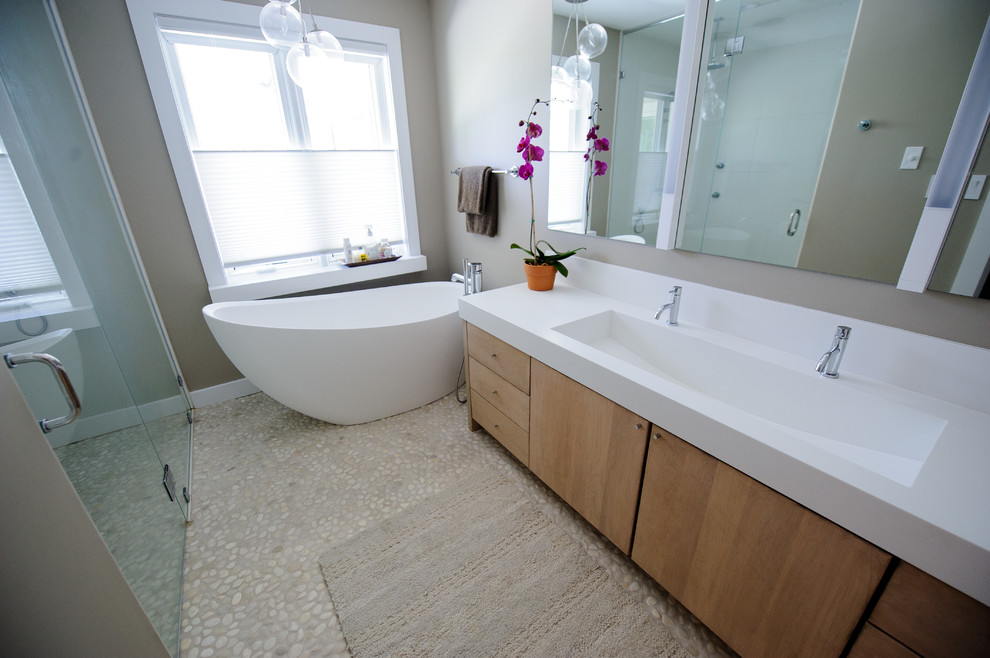 Exempel på ett mellanstort modernt en-suite badrum, med ett avlångt handfat, släta luckor, skåp i ljust trä, bänkskiva i akrylsten, ett fristående badkar, en kantlös dusch, beige kakel, kakel i småsten och grå väggar