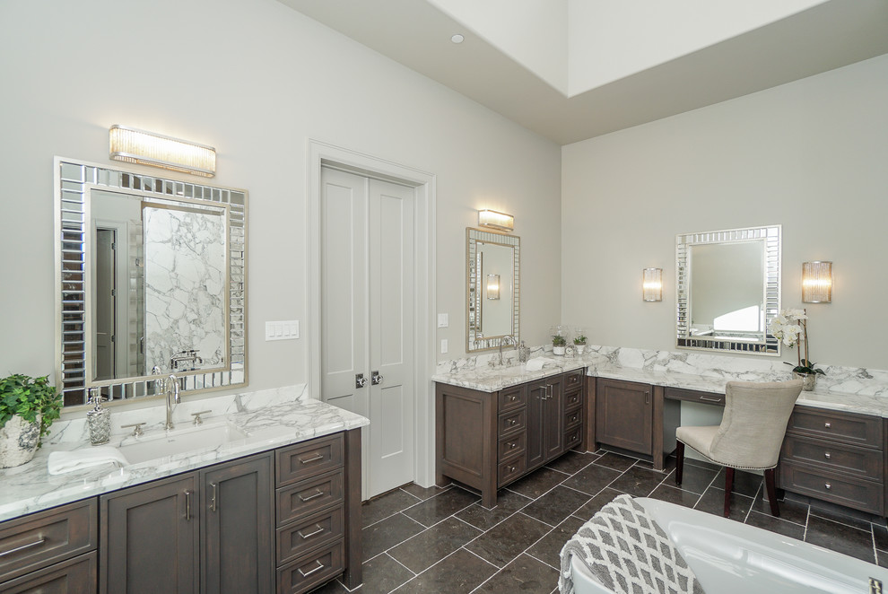This is an example of a large traditional ensuite bathroom in Houston with shaker cabinets, dark wood cabinets, a freestanding bath, grey walls, porcelain flooring, a submerged sink, marble worktops, brown floors and white worktops.