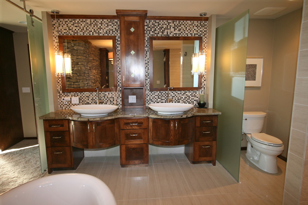 Diseño de cuarto de baño actual con lavabo sobreencimera, puertas de armario de madera oscura, bañera exenta, baldosas y/o azulejos beige y suelo de baldosas de porcelana