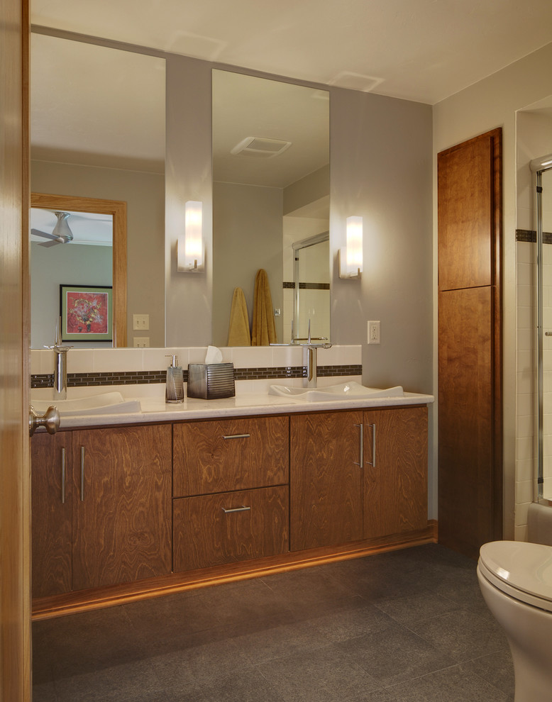 Design ideas for a small midcentury ensuite bathroom in Milwaukee with a vessel sink, flat-panel cabinets, medium wood cabinets, engineered stone worktops, an alcove bath, a shower/bath combination, a one-piece toilet, white tiles, metro tiles, grey walls and porcelain flooring.