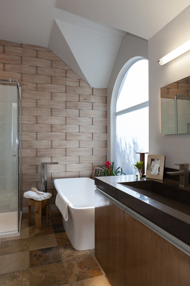 Idées déco pour une douche en alcôve principale contemporaine en bois brun de taille moyenne avec un placard à porte plane, une baignoire indépendante, un carrelage beige, du carrelage en ardoise, un mur beige, un sol en ardoise, une grande vasque et un plan de toilette en surface solide.