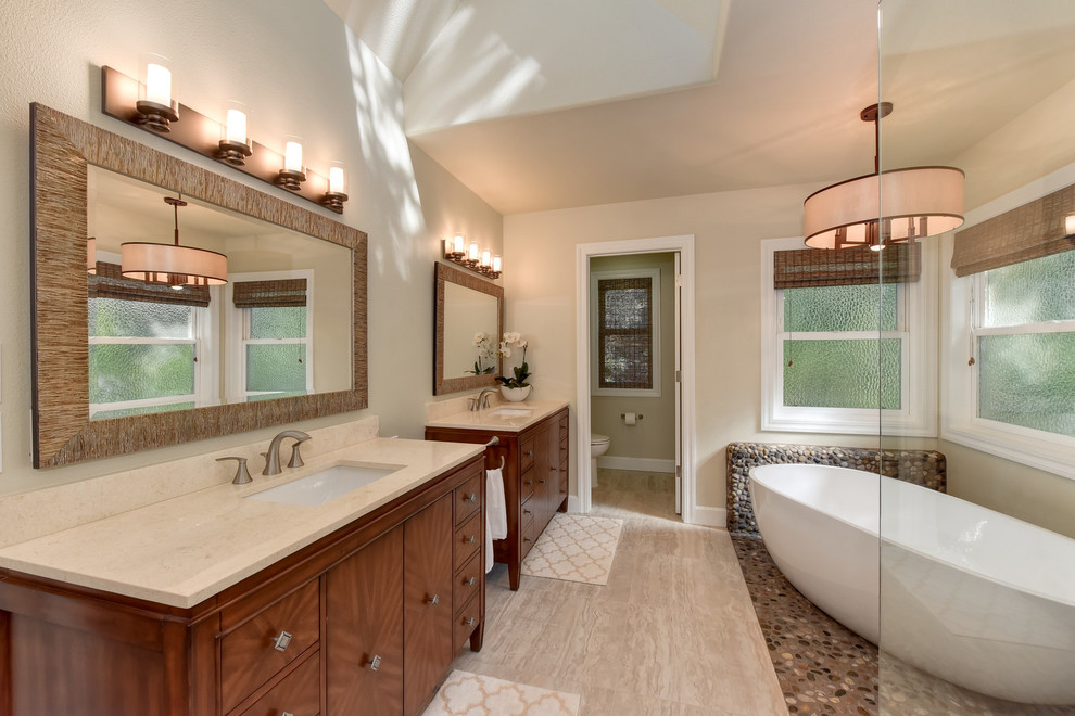 Photo of a large classic ensuite bathroom in Sacramento with flat-panel cabinets, medium wood cabinets, a freestanding bath, a corner shower, a two-piece toilet, brown tiles, pebble tiles, beige walls, a submerged sink, quartz worktops, porcelain flooring, beige floors and an open shower.