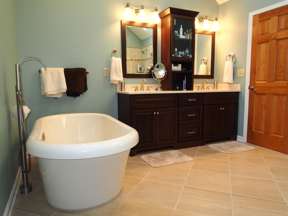 Пример оригинального дизайна: большая ванная комната в стиле неоклассика (современная классика) с врезной раковиной, фасадами с выступающей филенкой, темными деревянными фасадами, столешницей из искусственного кварца, отдельно стоящей ванной, двойным душем, унитазом-моноблоком, бежевой плиткой, керамогранитной плиткой, синими стенами и полом из известняка