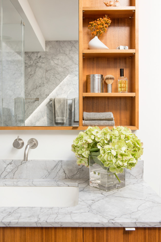 Inspiration for a medium sized contemporary ensuite bathroom in New York with flat-panel cabinets, medium wood cabinets, a submerged bath, grey tiles, stone slabs, white walls, porcelain flooring, a submerged sink and marble worktops.