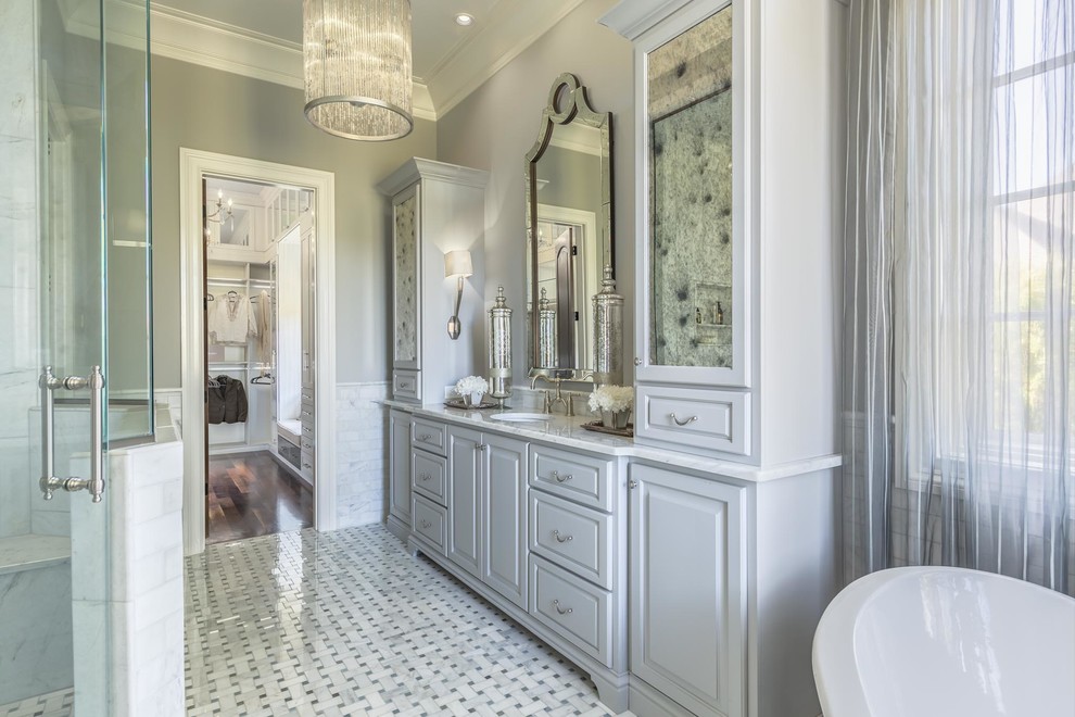 Inspiration for a large classic ensuite bathroom in Nashville with freestanding cabinets, grey cabinets, a freestanding bath, an alcove shower, a two-piece toilet, white tiles, ceramic tiles, grey walls, ceramic flooring, a submerged sink, marble worktops, grey floors and a hinged door.