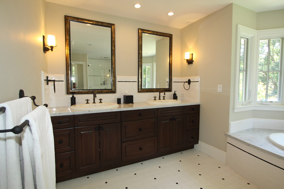 Modelo de cuarto de baño clásico con lavabo encastrado, armarios con paneles con relieve, puertas de armario de madera en tonos medios, bañera encastrada y baldosas y/o azulejos blancos