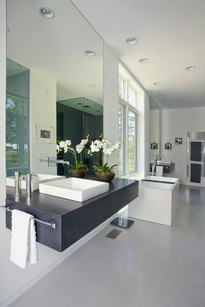 Пример оригинального дизайна: большая главная ванная комната в современном стиле с серыми фасадами, отдельно стоящей ванной, белой плиткой, белыми стенами, бетонным полом, накладной раковиной и столешницей из гранита