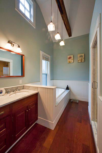 Cette image montre une douche en alcôve principale traditionnelle de taille moyenne avec un lavabo intégré, un placard à porte shaker, des portes de placard blanches, un mur beige, un sol en bois brun et une baignoire posée.