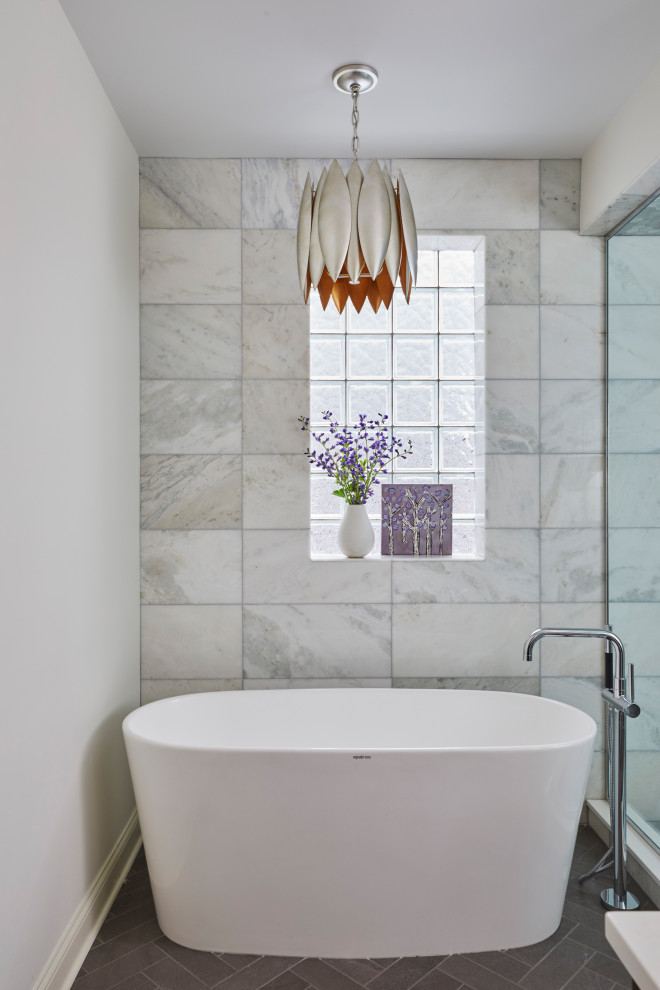 Cette photo montre une salle de bain principale bord de mer de taille moyenne avec une baignoire indépendante, une douche ouverte, un carrelage gris, du carrelage en marbre, un mur blanc, un sol en marbre, un sol marron et une cabine de douche à porte battante.