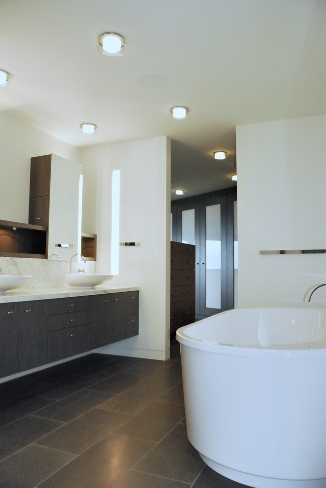 Пример оригинального дизайна: большая главная ванная комната в современном стиле с настольной раковиной, плоскими фасадами, темными деревянными фасадами, мраморной столешницей, отдельно стоящей ванной, душем в нише, инсталляцией, белой плиткой, стеклянной плиткой, белыми стенами, полом из керамогранита и серым полом