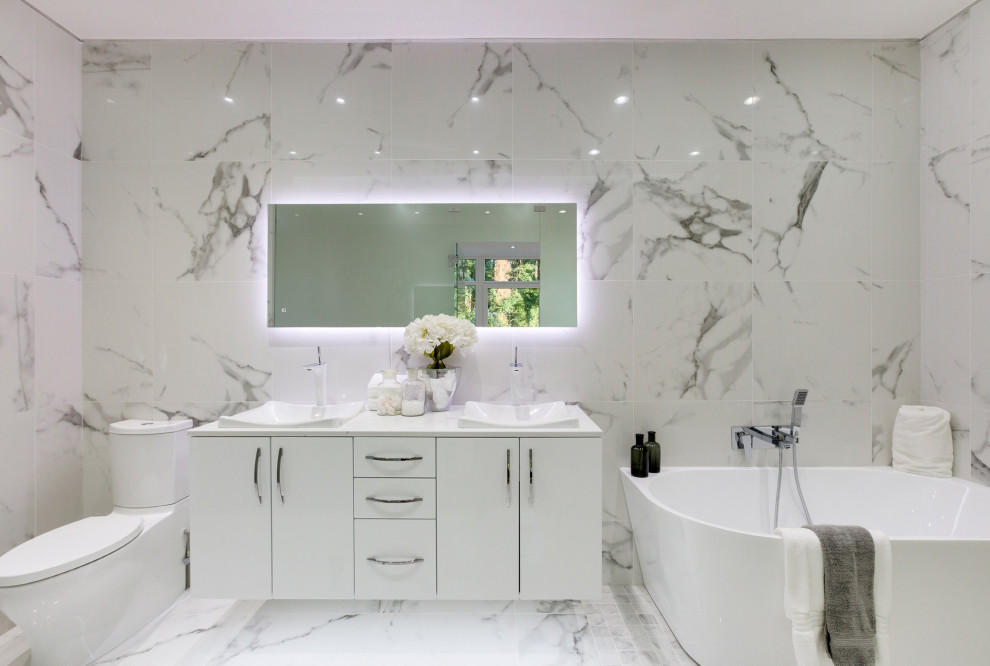 Inspiration for a contemporary bathroom in Seattle with flat-panel cabinets, white cabinets, a freestanding bath, a two-piece toilet, white tiles, a built-in sink, white floors, white worktops, double sinks and a floating vanity unit.