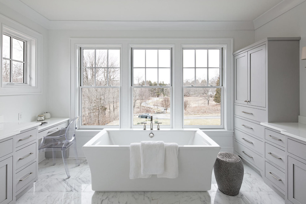 Imagen de cuarto de baño principal clásico con puertas de armario grises, suelo de mármol, armarios estilo shaker, bañera exenta, baldosas y/o azulejos blancos y paredes blancas