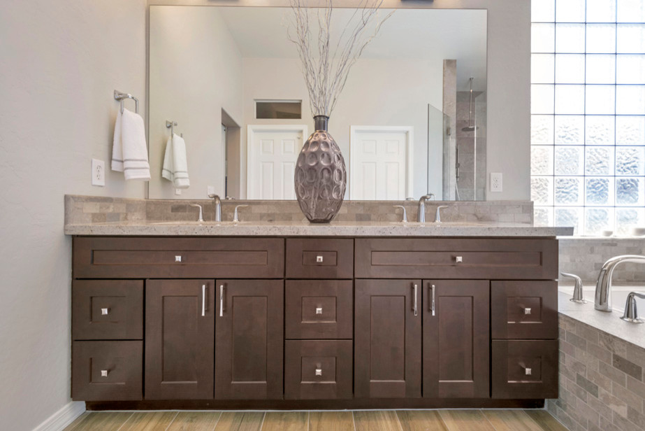 Large traditional ensuite bathroom in Phoenix with raised-panel cabinets, brown cabinets, a built-in bath, a corner shower, beige tiles, porcelain tiles, grey walls, porcelain flooring, a built-in sink, granite worktops, brown floors and a hinged door.
