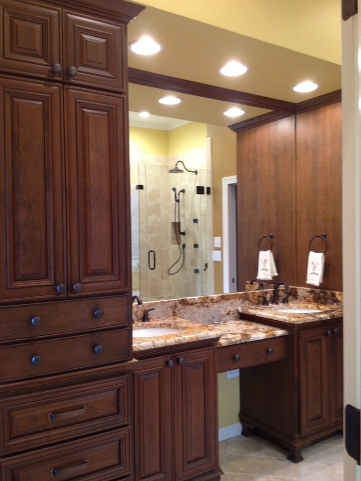 This is an example of a large traditional ensuite bathroom in Charlotte with a submerged sink, freestanding cabinets, medium wood cabinets, granite worktops, a freestanding bath, a walk-in shower, a two-piece toilet, beige tiles, stone tiles, beige walls and travertine flooring.