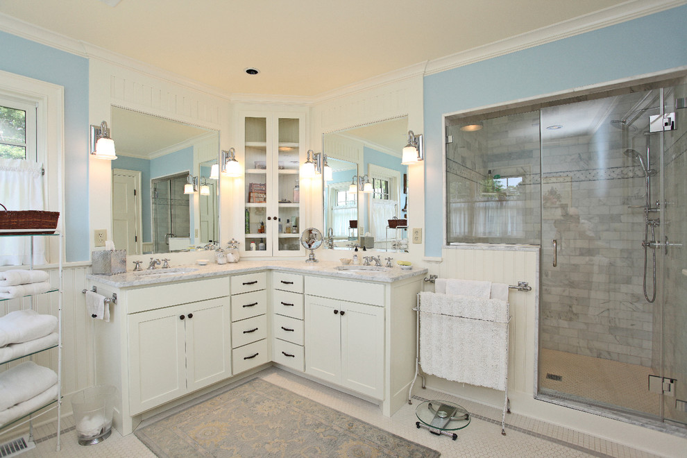 Modelo de cuarto de baño de estilo de casa de campo con lavabo bajoencimera, ducha empotrada, puertas de armario blancas, armarios con paneles empotrados, encimera de mármol, paredes azules y suelo de mármol