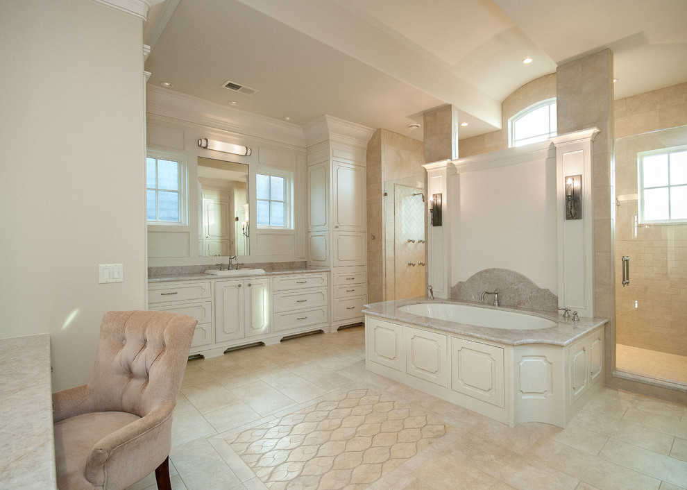 Aménagement d'une très grande salle de bain principale classique avec un lavabo posé, un placard avec porte à panneau surélevé, des portes de placard blanches, un plan de toilette en granite, une baignoire encastrée, un carrelage beige, un carrelage de pierre, un mur blanc et un sol en travertin.