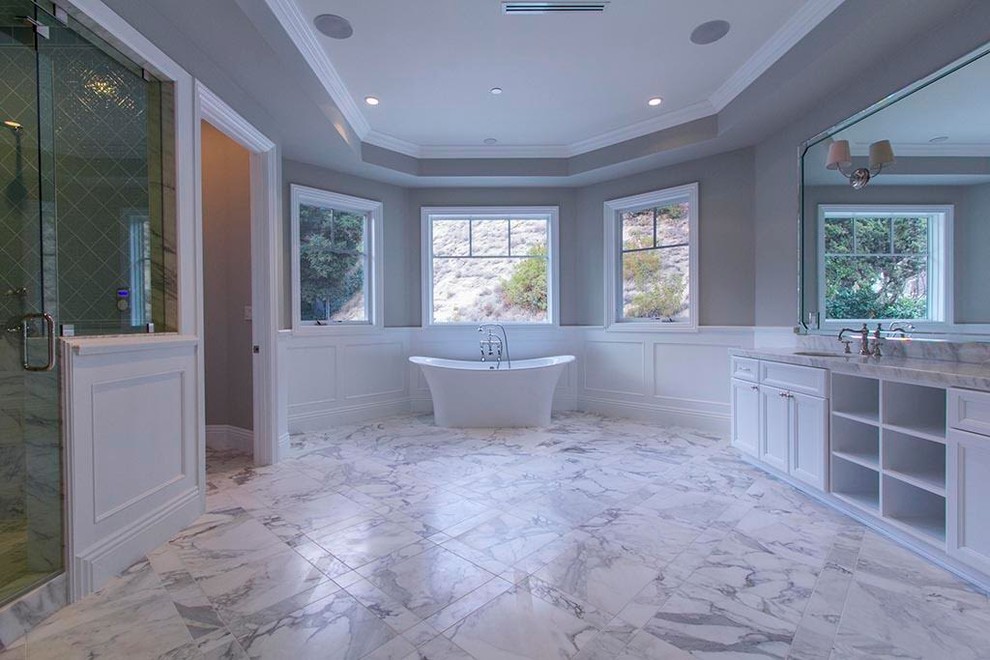 This is an example of an expansive traditional ensuite bathroom in Los Angeles with white cabinets, a freestanding bath, marble flooring, a submerged sink, marble worktops, recessed-panel cabinets, an alcove shower, a two-piece toilet, grey walls, grey floors and a hinged door.
