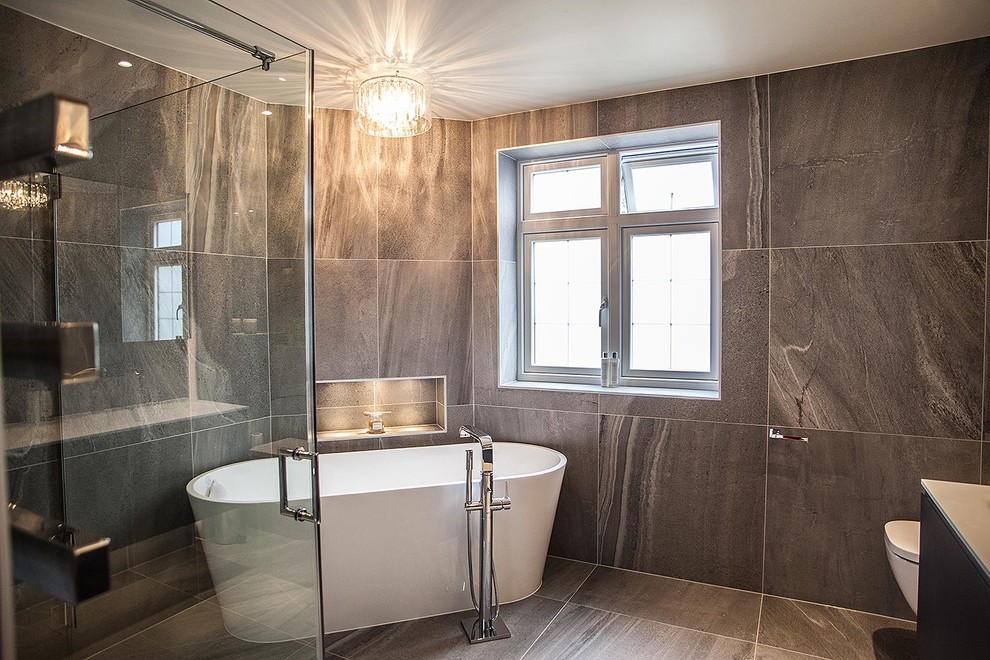 Exempel på ett stort modernt badrum, med ett fristående badkar, en öppen dusch, en vägghängd toalettstol, grå kakel, porslinskakel, grå väggar, klinkergolv i porslin och ett nedsänkt handfat