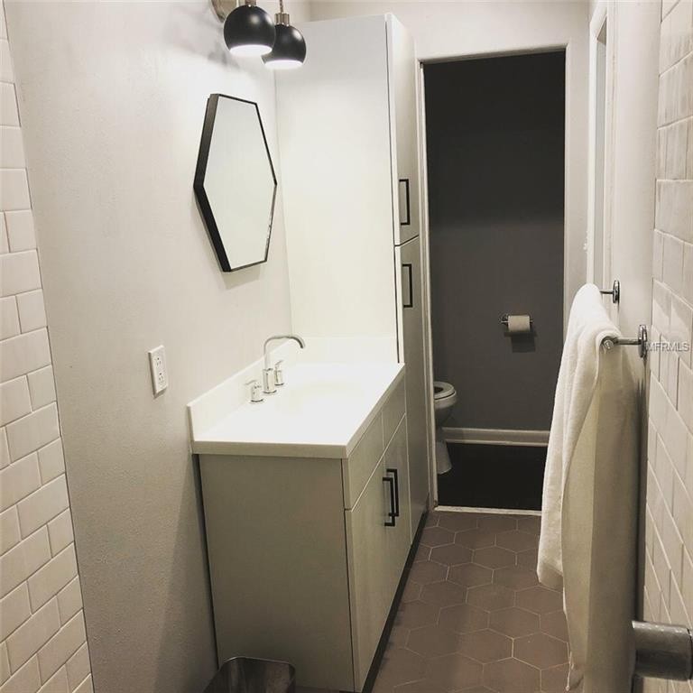 Cette photo montre une petite salle de bain principale rétro avec un placard à porte plane, des portes de placard blanches, un espace douche bain, WC à poser, un carrelage blanc, un carrelage métro, un mur gris, un sol en carrelage de porcelaine, un lavabo intégré, un plan de toilette en surface solide, un sol gris, aucune cabine et un plan de toilette blanc.