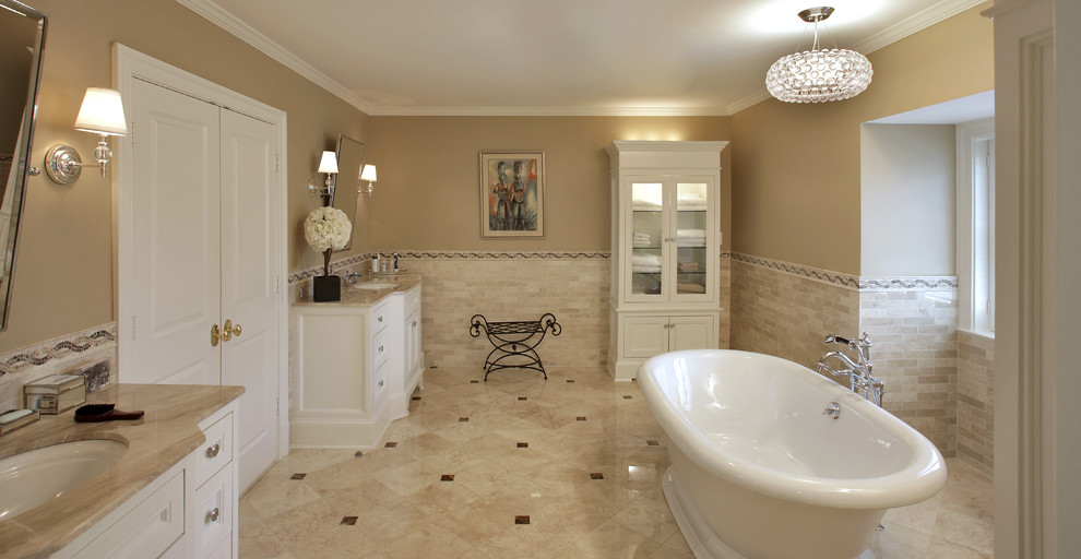 Amerikansk inredning av ett stort en-suite badrum, med ett undermonterad handfat, luckor med infälld panel, vita skåp, granitbänkskiva, ett fristående badkar, beige kakel, stenkakel, beige väggar och marmorgolv