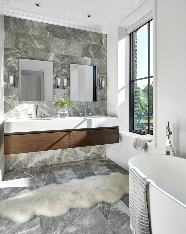 Inredning av ett klassiskt mellanstort en-suite badrum, med släta luckor, ett fristående badkar, grå kakel, stenkakel, ett undermonterad handfat, bänkskiva i akrylsten, grått golv, skåp i mörkt trä och vita väggar
