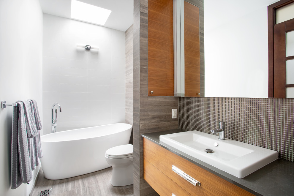 Mid-sized trendy master porcelain tile and gray floor bathroom photo in Other with flat-panel cabinets, medium tone wood cabinets, a one-piece toilet, white walls, a drop-in sink and a hinged shower door