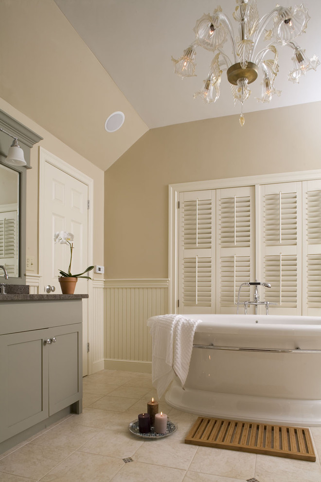 Cette image montre une salle de bain traditionnelle avec une baignoire indépendante, un carrelage beige et des portes de placard grises.