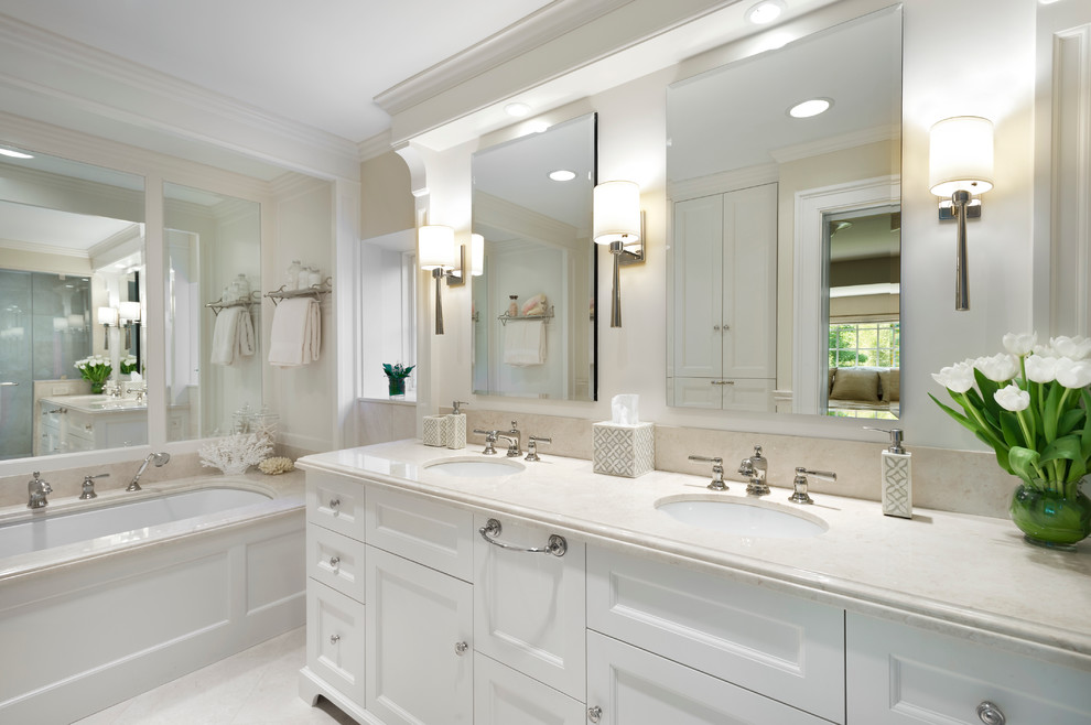 Klassisk inredning av ett litet badrum, med ett undermonterad handfat, vita skåp, marmorbänkskiva, ett undermonterat badkar, svart kakel, stenhäll, vita väggar och marmorgolv