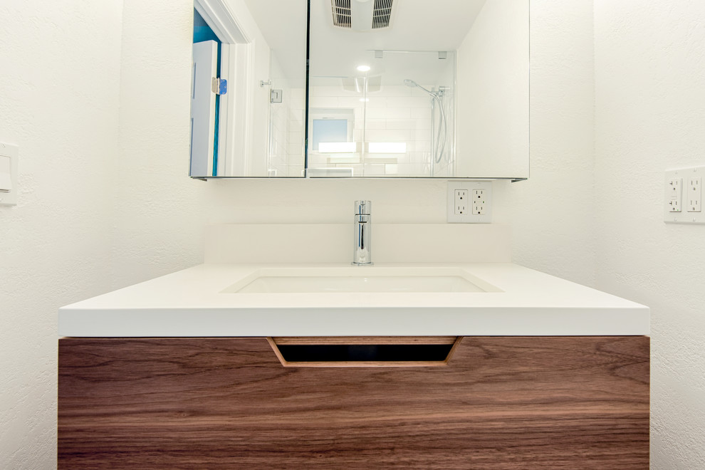 Photo of a large modern ensuite bathroom in San Francisco with flat-panel cabinets, brown cabinets, a built-in bath, a walk-in shower, a wall mounted toilet, white tiles, metro tiles, white walls, mosaic tile flooring, a built-in sink, quartz worktops, black floors, a hinged door and white worktops.
