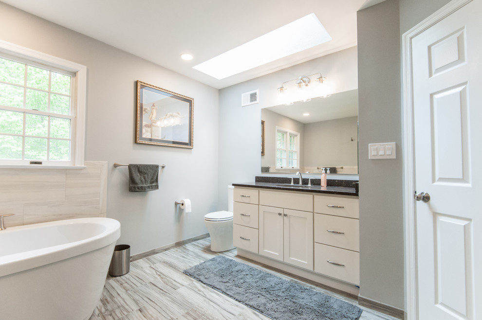 This is an example of a medium sized coastal ensuite bathroom in DC Metro with shaker cabinets, beige cabinets, a freestanding bath, a one-piece toilet, beige tiles, porcelain tiles, blue walls, porcelain flooring, a submerged sink, engineered stone worktops, brown worktops, a single sink and a built in vanity unit.