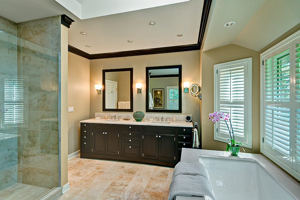 Large traditional bathroom in Chicago with a submerged sink, recessed-panel cabinets, dark wood cabinets, marble worktops, a submerged bath, an alcove shower, a one-piece toilet, beige tiles, stone tiles, beige walls and limestone flooring.
