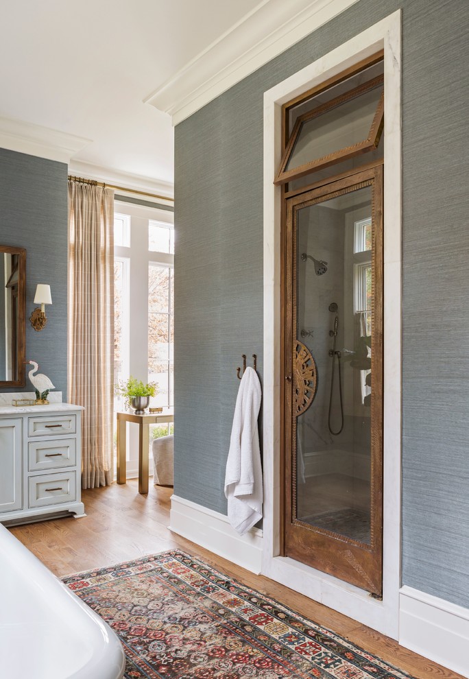 Design ideas for a large world-inspired ensuite bathroom in Little Rock with shaker cabinets, white cabinets, a freestanding bath, an alcove shower, blue walls, medium hardwood flooring, granite worktops, brown floors, a hinged door and white worktops.