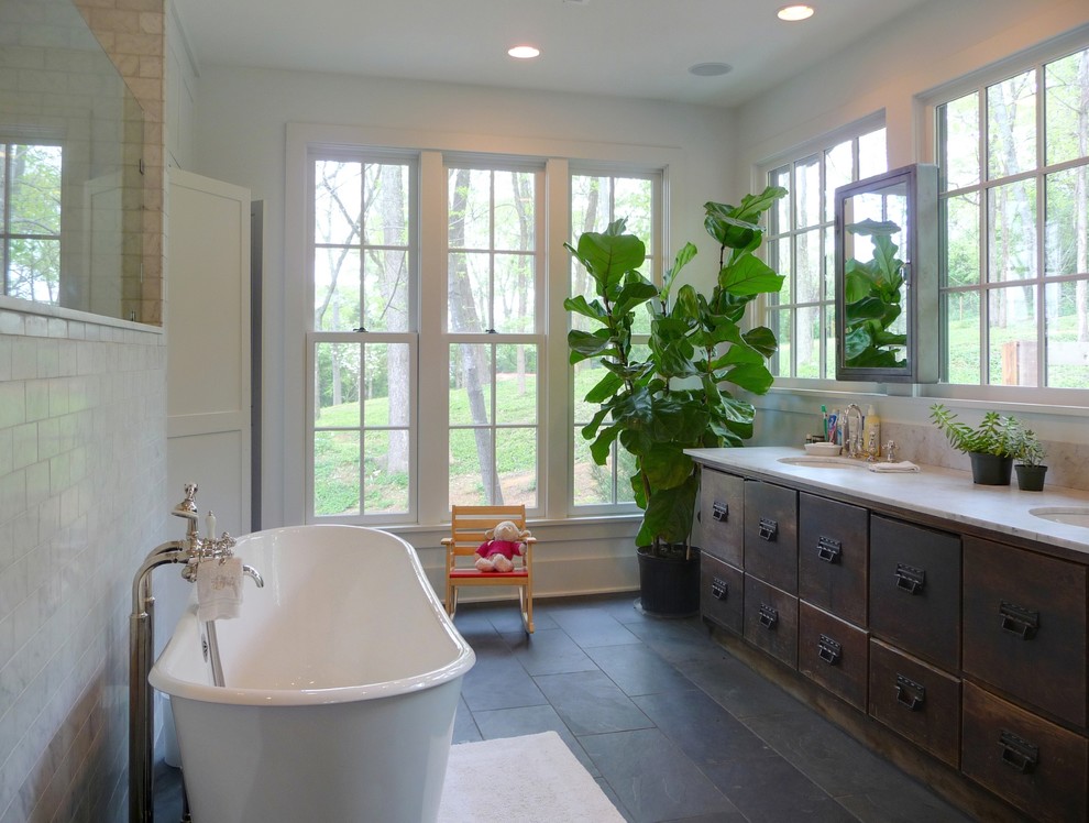 На фото: ванная комната в современном стиле с врезной раковиной, плоскими фасадами, искусственно-состаренными фасадами, отдельно стоящей ванной, серой плиткой, полом из сланца и фартуком