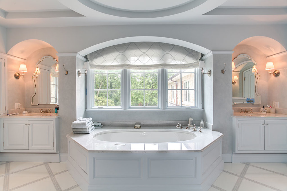 Immagine di una grande stanza da bagno padronale chic con ante con bugna sagomata, ante bianche, vasca da incasso, pareti bianche, lavabo sottopiano, top in marmo e pavimento bianco
