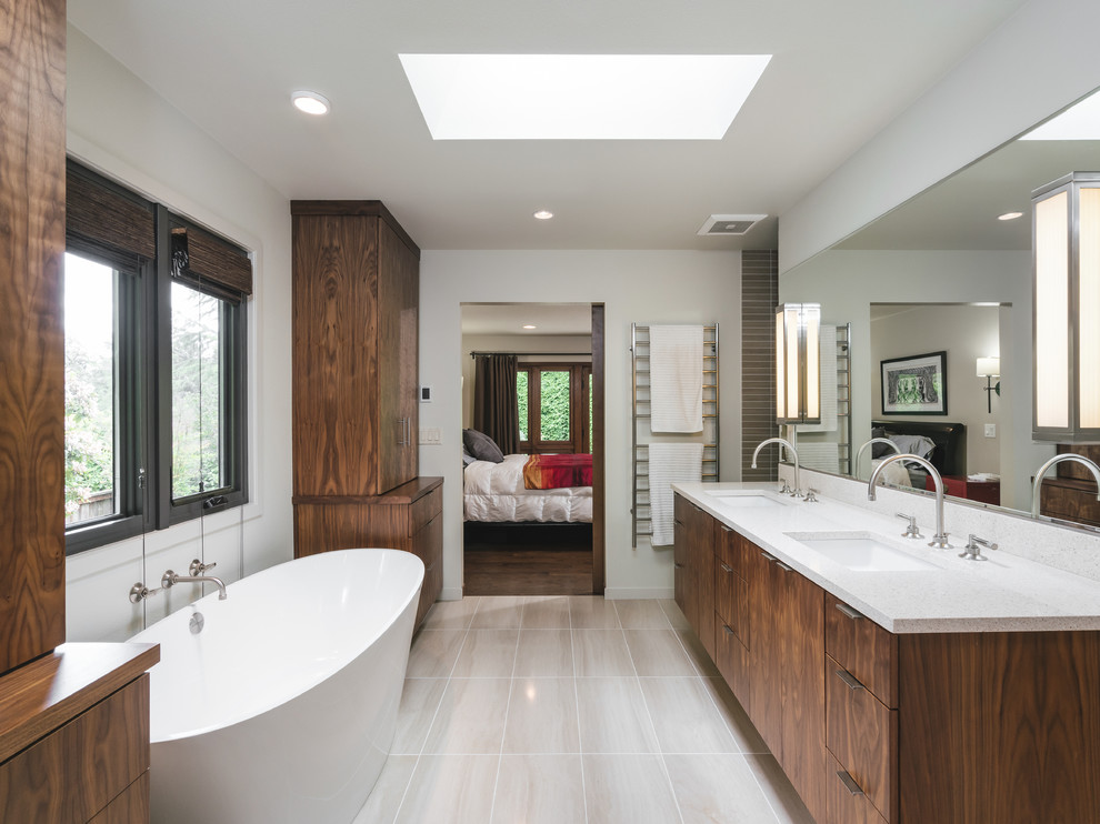 Diseño de cuarto de baño retro con armarios con paneles lisos, puertas de armario de madera en tonos medios, bañera exenta, paredes blancas, lavabo bajoencimera, suelo gris y encimeras blancas
