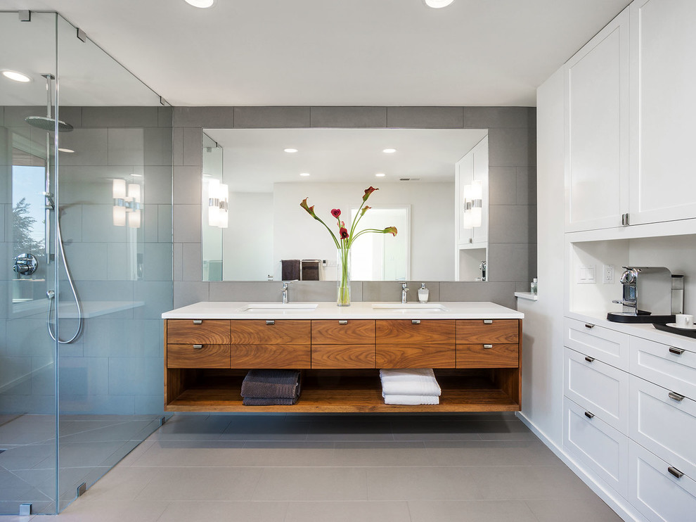 Стильный дизайн: ванная комната в современном стиле с плоскими фасадами, фасадами цвета дерева среднего тона, душем без бортиков, серой плиткой и врезной раковиной - последний тренд
